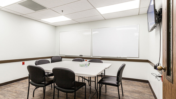 Interior conference room with white table, black chairs, large whiteboards, and mounted television