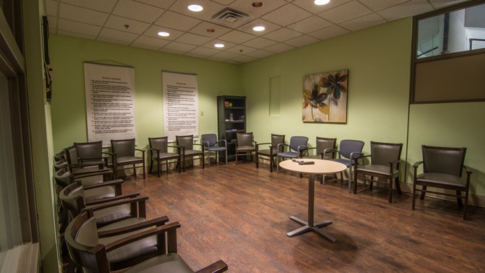 Interior group therapy space with lime green walls, multiple brown upholstered chairs arranged in semicircle, and informational posters on walls