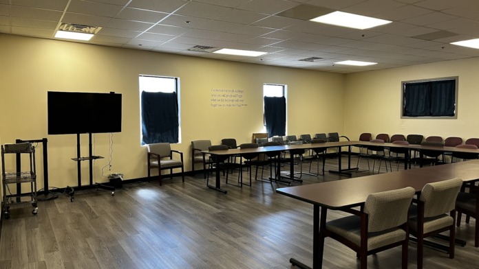 Interior group therapy room with multiple tables, chairs, presentation screen, and windows with natural lighting