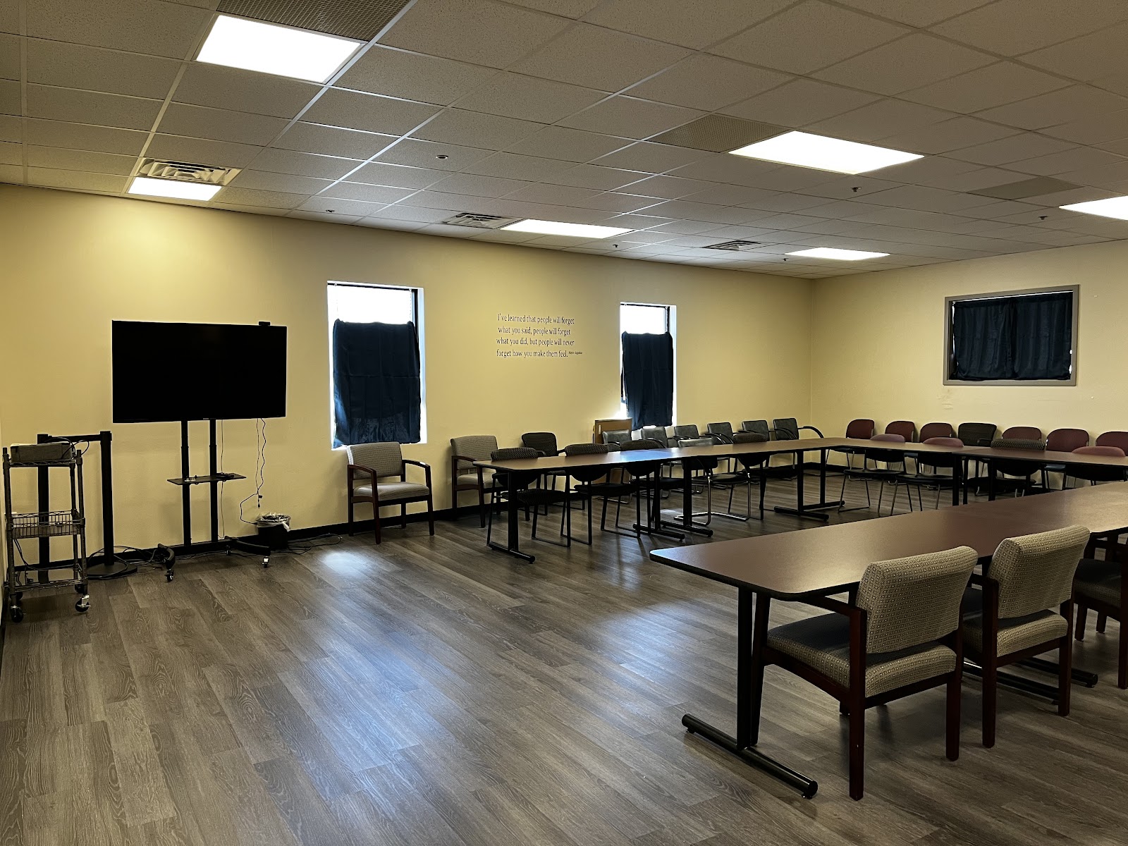 Interior group therapy room with multiple tables, chairs, presentation screen, and windows with natural lighting