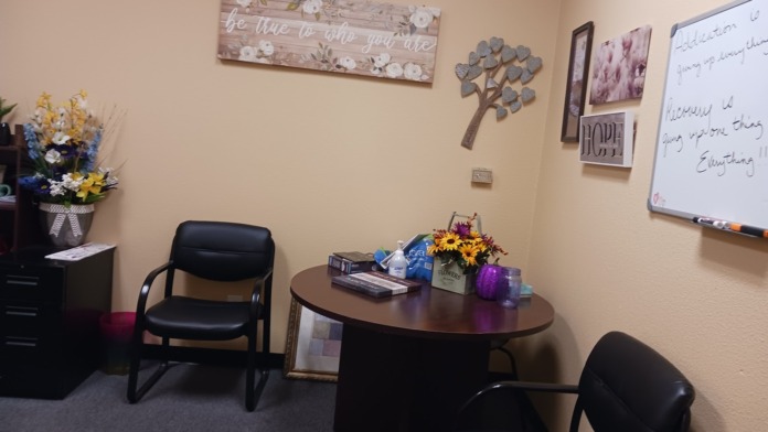 Interior therapy room with round table, black chairs, decorative wall art, flowers, and whiteboard
