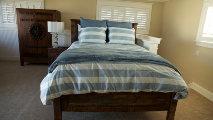 Interior bedroom featuring queen bed with blue striped bedding, large window with ocean vista, wood furnishings, and coastal decor