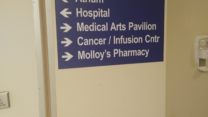 Interior hospital hallway with blue and white directional sign indicating Atrium, Hospital, Medical Arts Pavilion, Cancer/Infusion Center, and Pharmacy locations