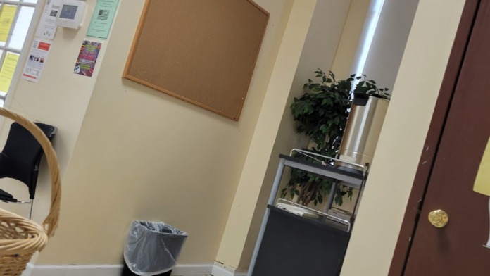 Interior hallway with cork bulletin board, wall-mounted clock, green plants, and office entry door