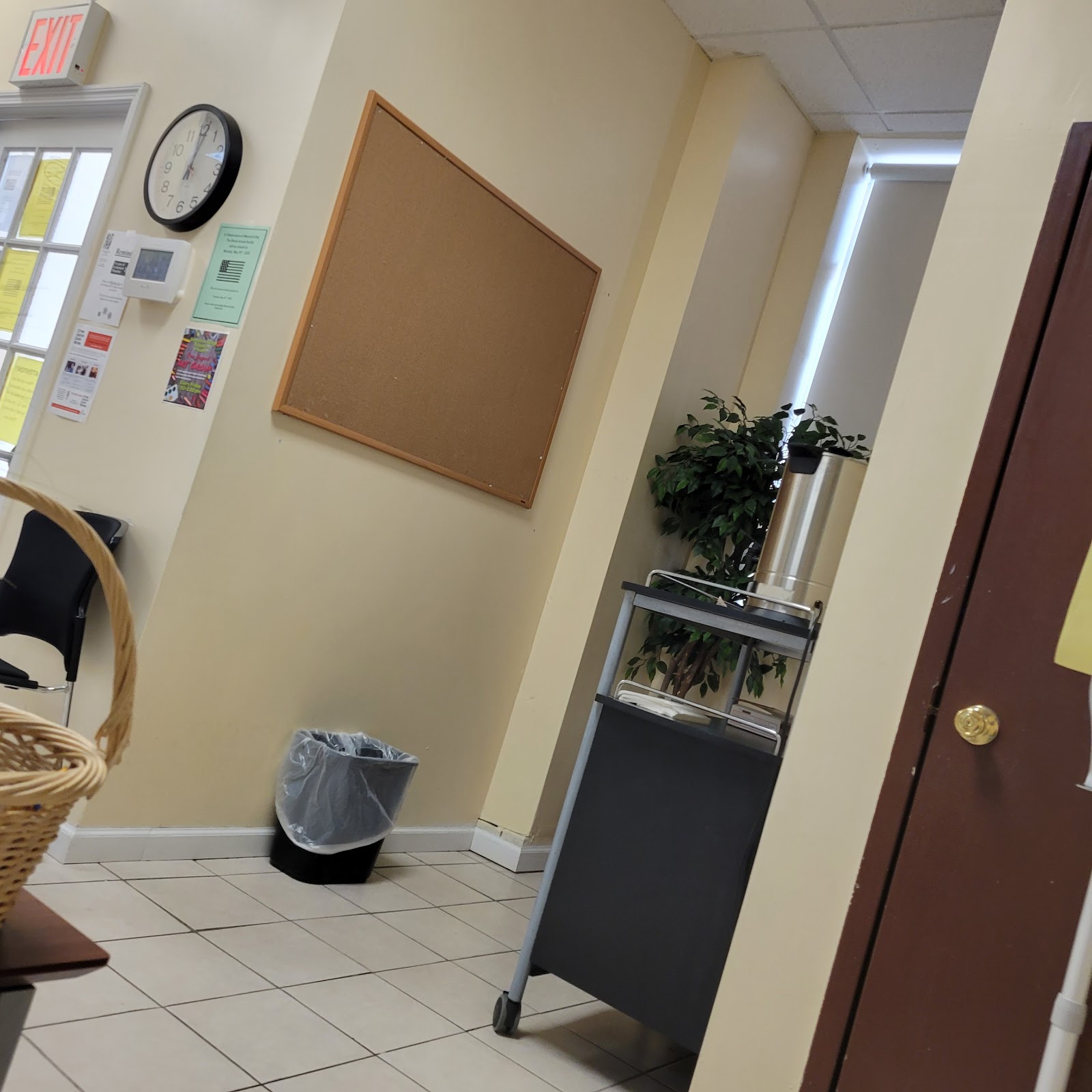 Interior hallway with cork bulletin board, wall-mounted clock, green plants, and office entry door
