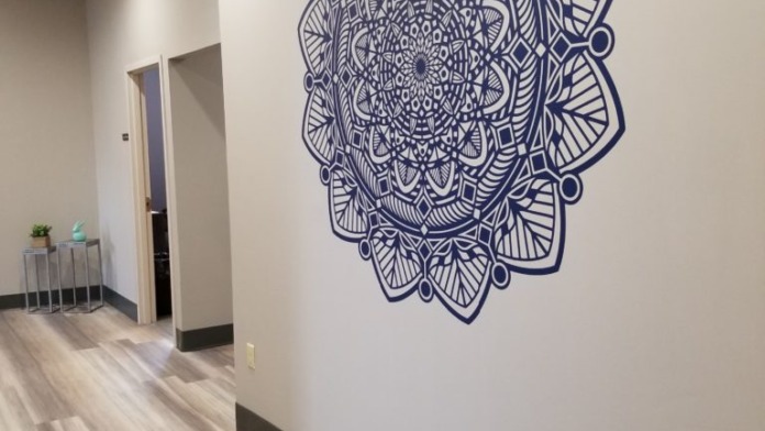 Interior hallway with light wood flooring, white walls, blue mandala wall design, and doorways
