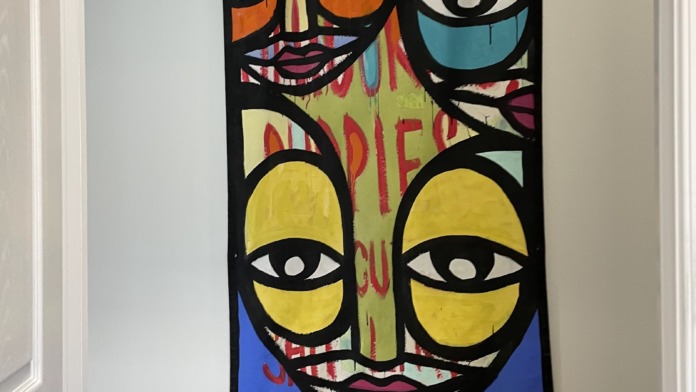 Interior hallway with colorful illustrated face artwork on wall, doorways, framed photographs, and religious crosses