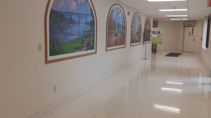 Interior hallway with white walls, framed landscape artwork with wooden frames, fluorescent lighting, and polished flooring