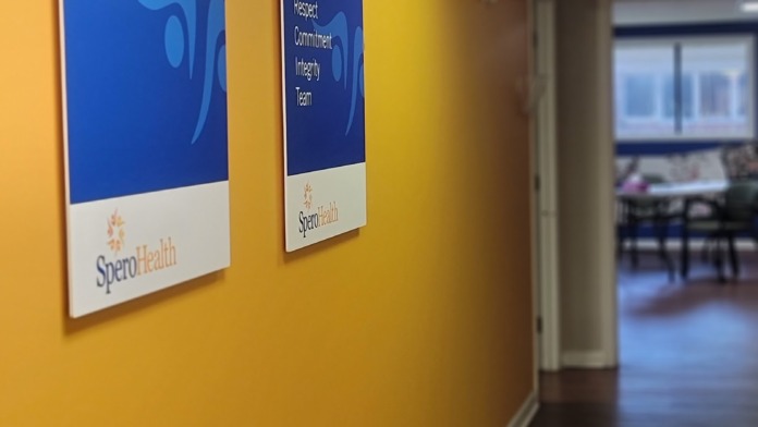 Interior hallway with bright yellow walls, blue mission and values posters with SperoHealth branding, and wooden flooring