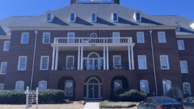 Exterior front facade of three-story brick building with white columns, arched windows, and manicured landscaping
