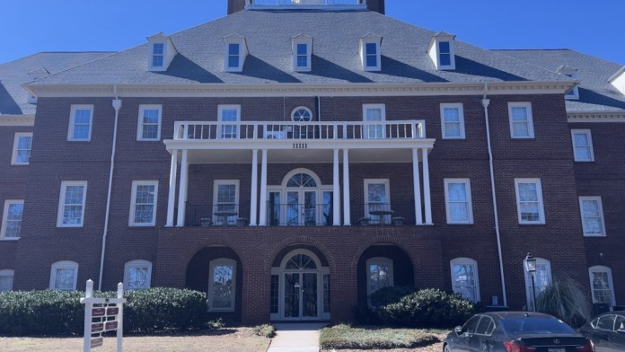 Exterior front facade of three-story brick building with white columns, arched windows, and manicured landscaping