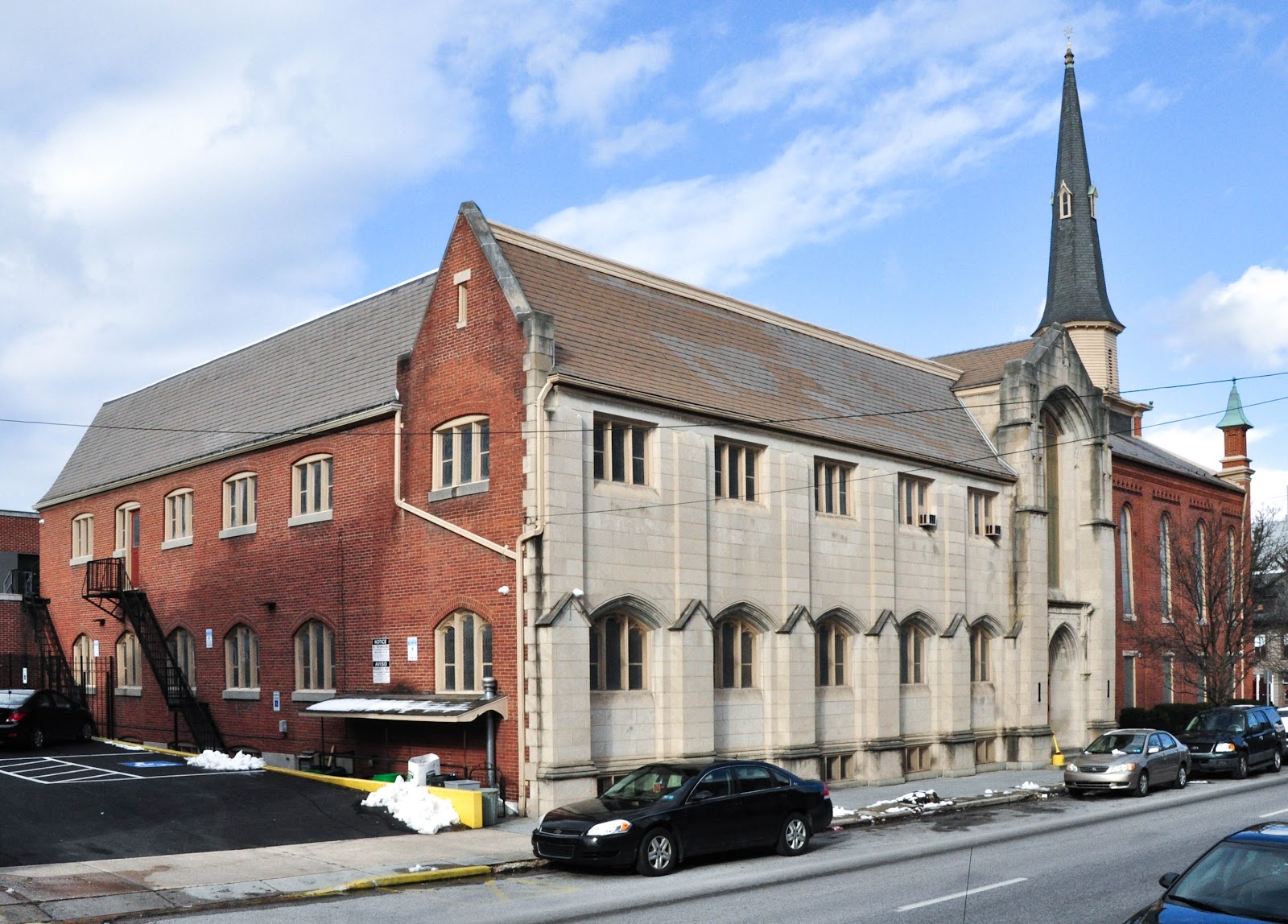 Exterior view of historic brick and stone buildings with parking area, multiple windows, and architectural details