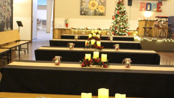 Interior fellowship hall with long serving tables, Christmas decorations, lit candles, and religious signage