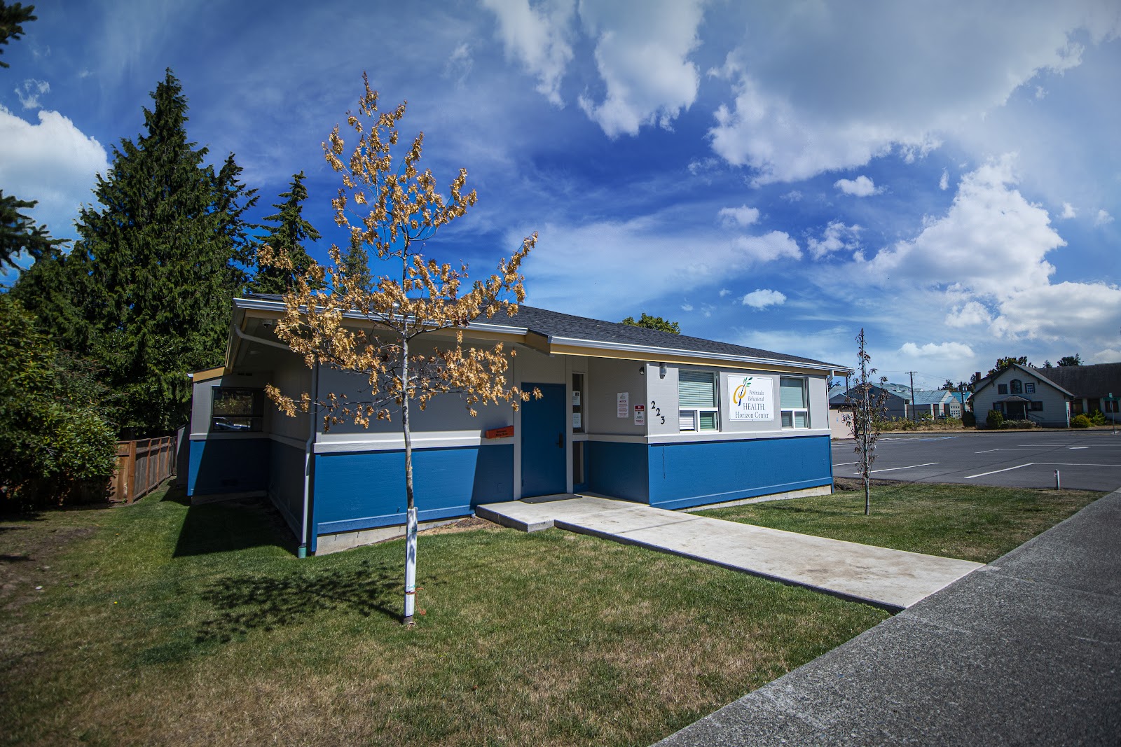 Exterior view of single-story treatment facility with blue and gray facade, landscaped grounds, and parking area