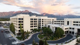 Exterior showing multi-building hospital complex with curved driveway, landscaping, and mountains visible at dusk