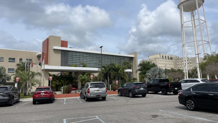 Exterior parking and main entrance showing modern facility building, water tower, and cloudy sky