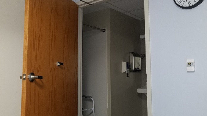 Interior office or break room doorway showing wooden door, wall clock, electrical outlets and switches in hallway area