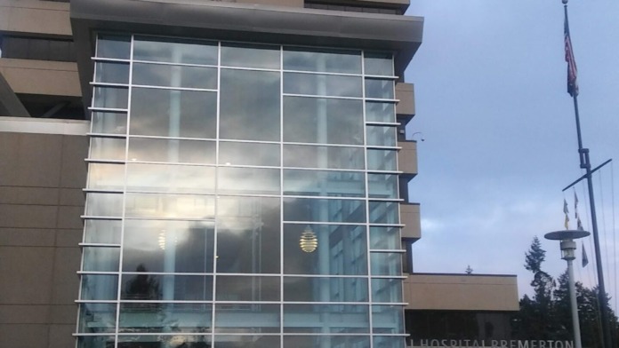 Exterior view of modern hospital building with large windows, tan facade, and flags on pole