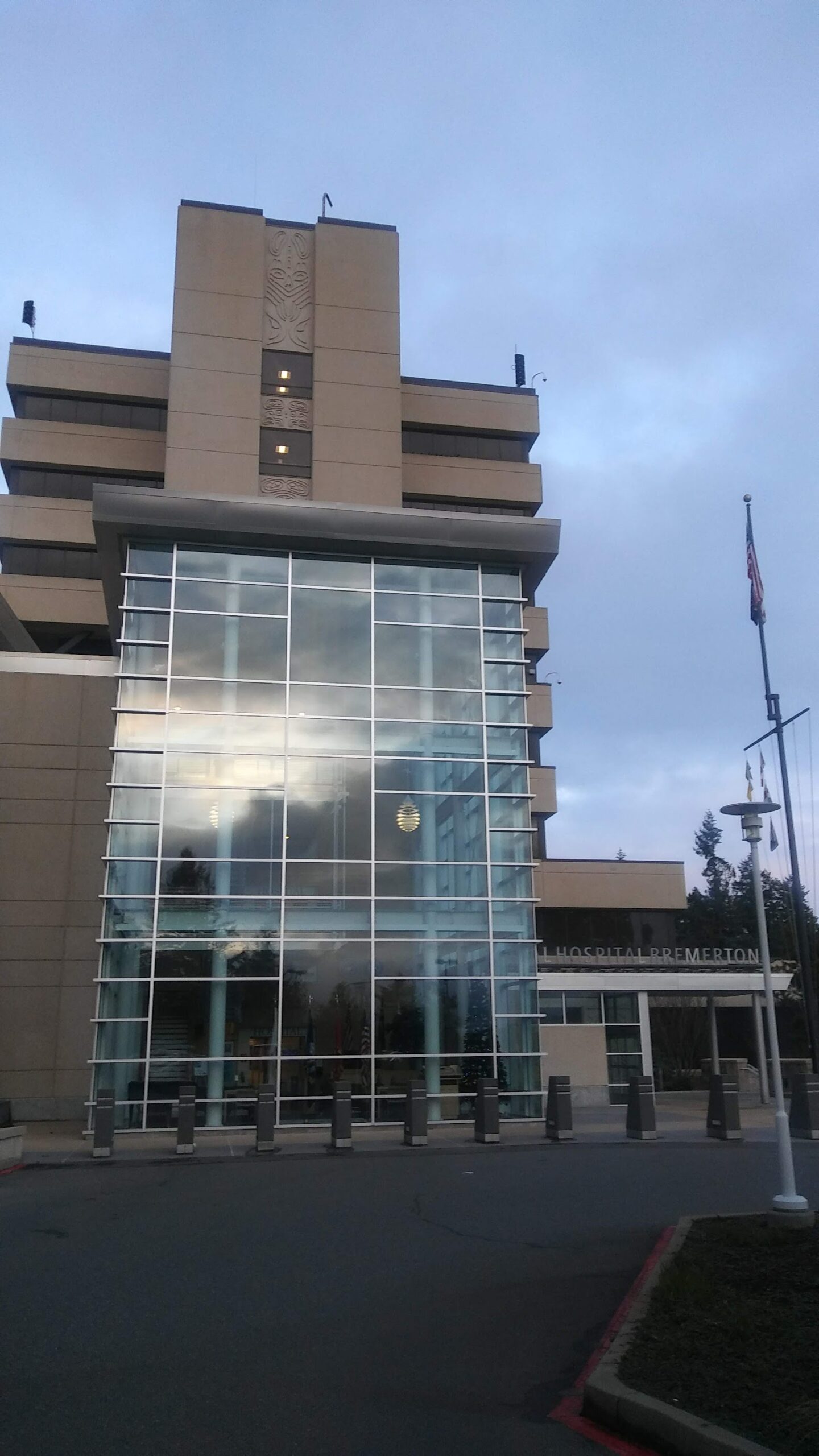 Exterior view of modern hospital building with large windows, tan facade, and flags on pole