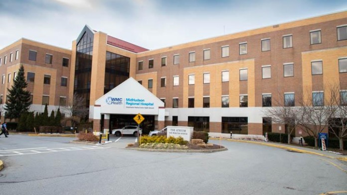 Exterior view of hospital main entrance showing brick and stone facade with covered entry, signage, and parking area