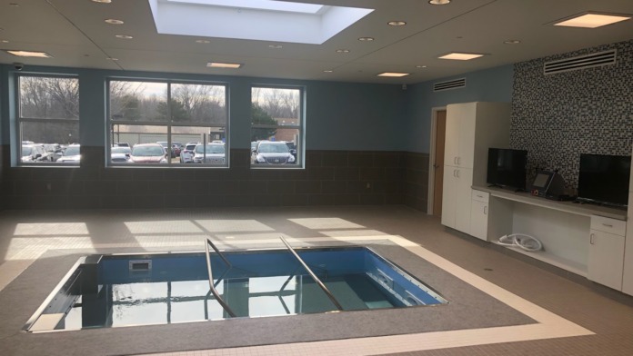 Interior aquatic therapy facility with indoor pool, large windows with natural light, and modern ceiling design