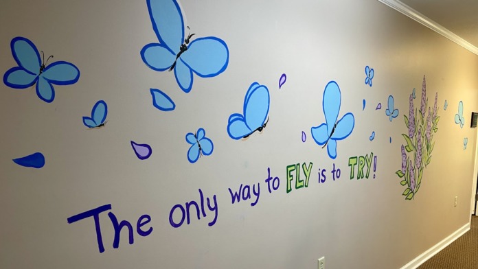 Interior hallway with motivational butterfly wall mural and text reading The only way to fly is to try