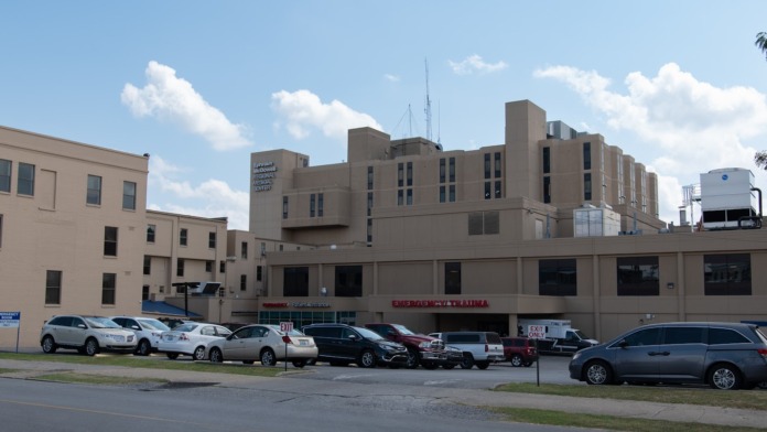 Exterior of large tan institutional building with parked vehicles in front lot
