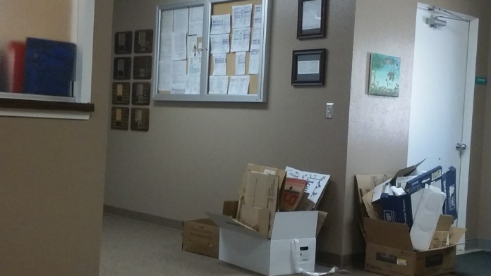 Interior hallway with bulletin board, informational signage, and storage boxes showing administrative spaces