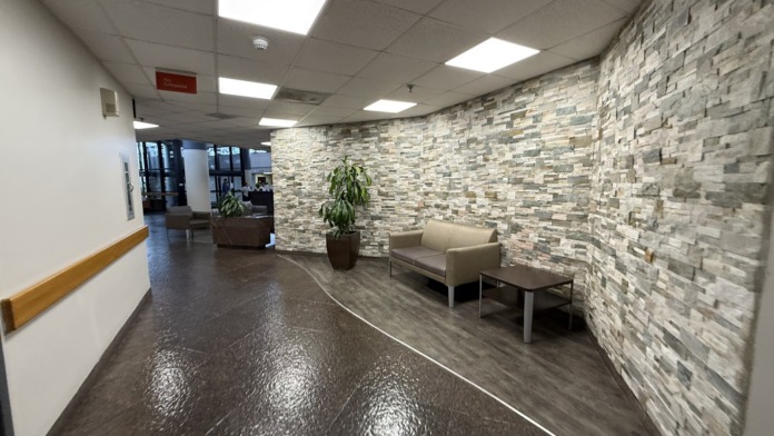 Interior hallway with stone brick accent wall, seating area, potted plant, LED ceiling panels, and modern minimalist design