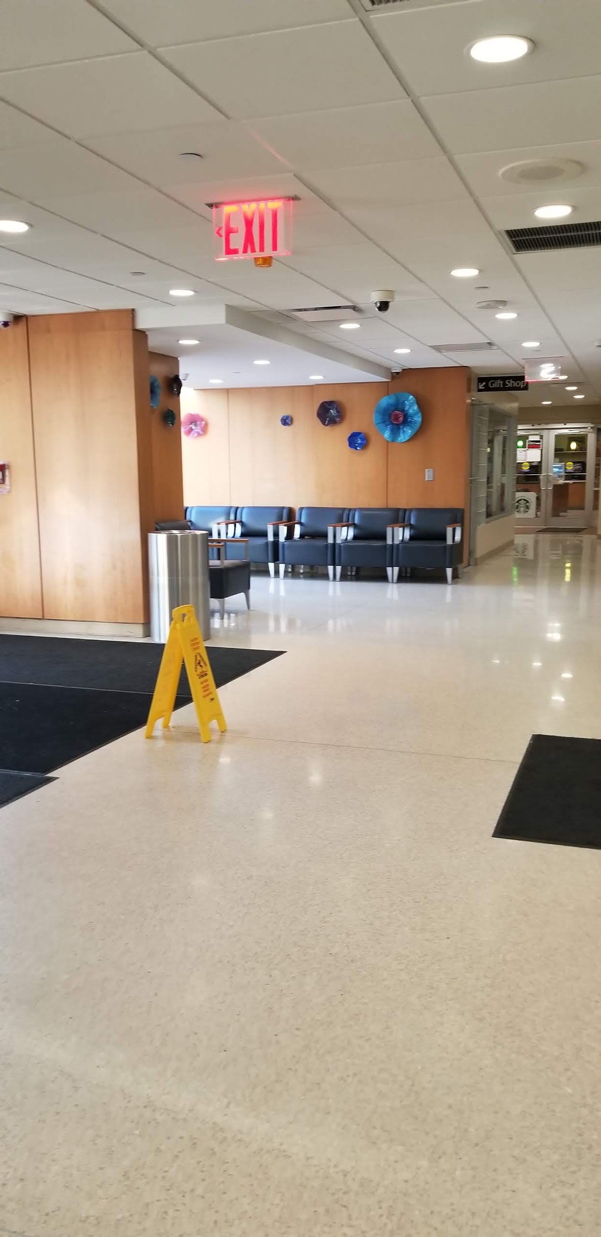 Interior hallway with blue seating chairs, decorative wall art, exit signage, and modern flooring