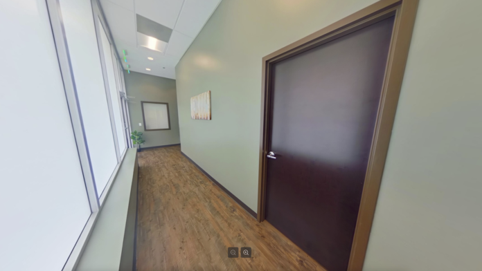 Interior hallway with light yellow walls, wooden flooring, closed brown door, minimal furnishings