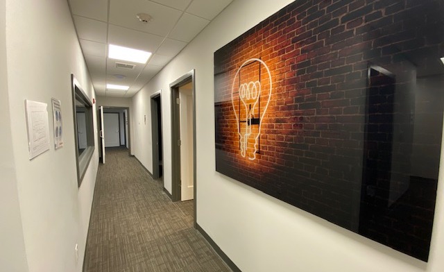 Interior hallway with white walls, brown carpet, multiple doorways, and neon lightbulb wall art