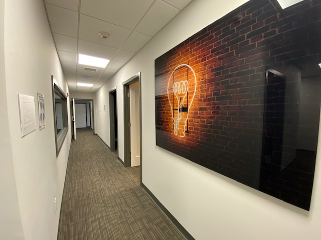 Interior hallway with white walls, brown carpet, multiple doorways, and neon lightbulb wall art