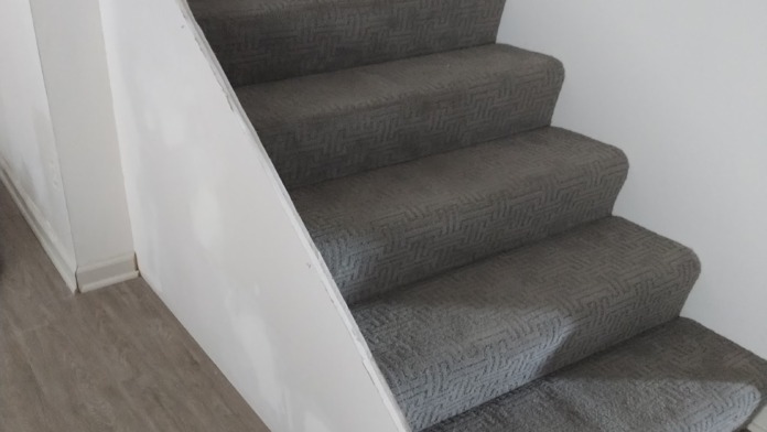 Interior staircase with gray patterned carpeting, white walls, and wooden handrail