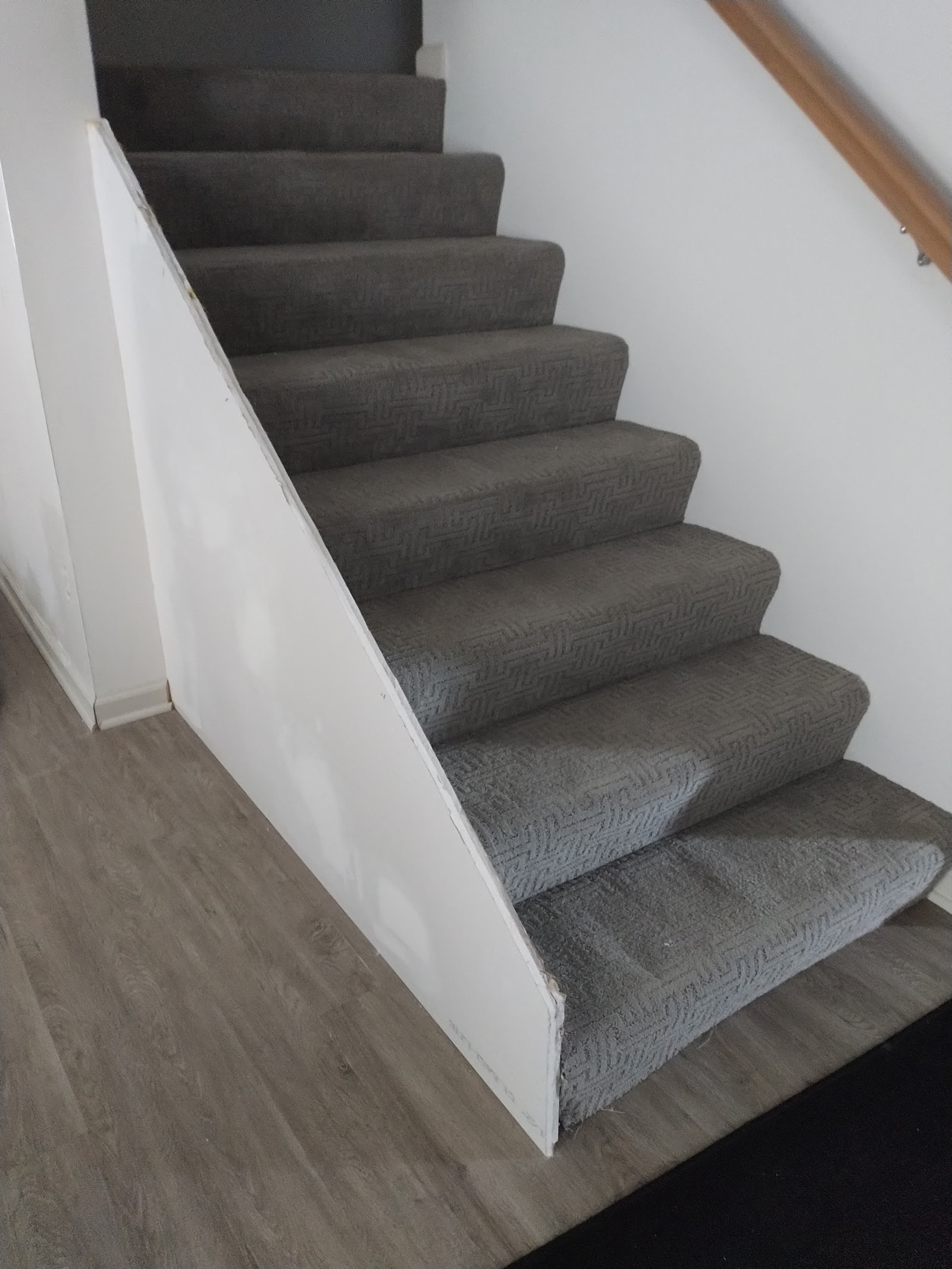 Interior staircase with gray patterned carpeting, white walls, and wooden handrail