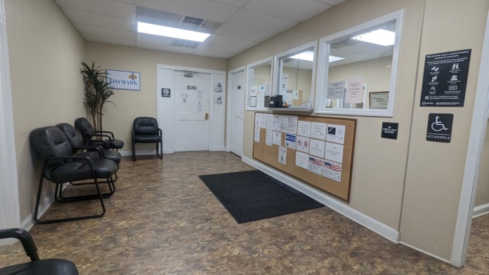 Interior waiting area with black upholstered chairs, cream-colored walls, window counter, and beige tile flooring