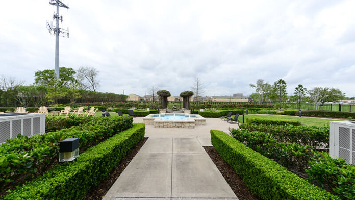 Outdoor walking path with manicured hedges, stone arbor structure, and well-maintained green landscape