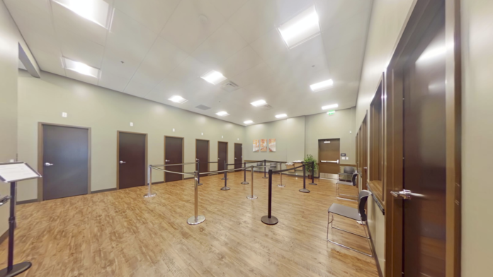 Interior large multi-purpose room with metal crowd control barriers, wooden floor, and brown doors