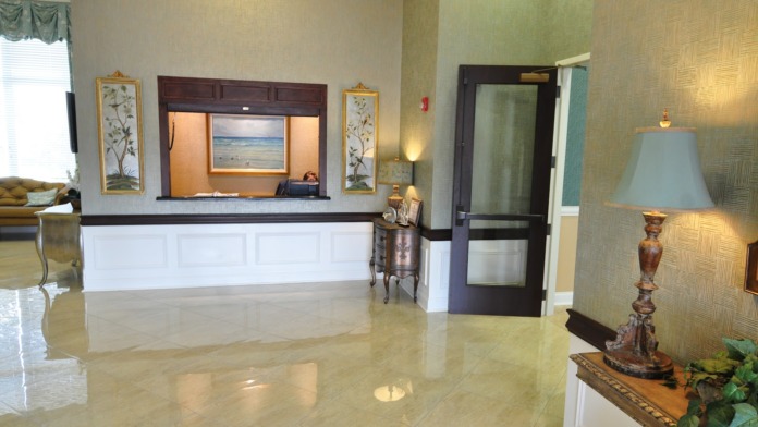 Interior lobby featuring dual-level desk with granite counter, painting artwork, decorative table, and view into facility spaces
