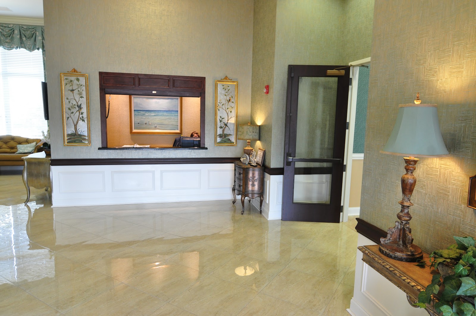 Interior lobby featuring dual-level desk with granite counter, painting artwork, decorative table, and view into facility spaces