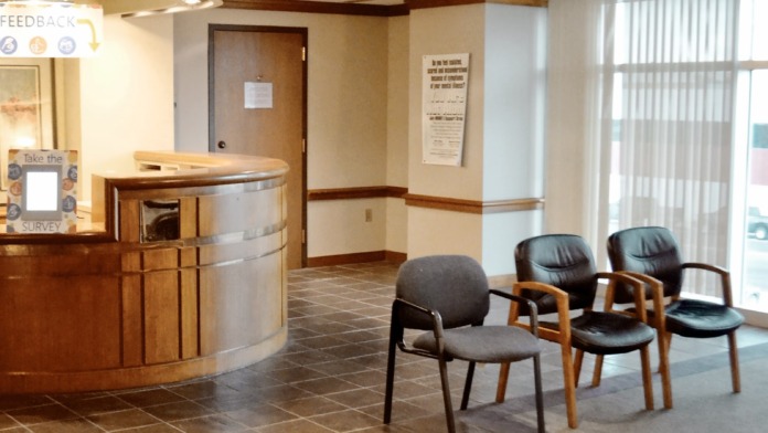 Interior lobby with curved wooden reception desk, seating chairs, and large windows with natural light