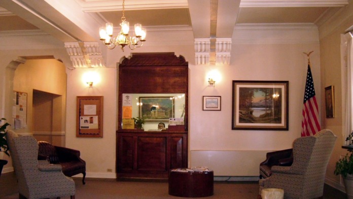 Interior lobby with chandelier lighting, seating areas, reception desk with natural wood trim, and wall artwork