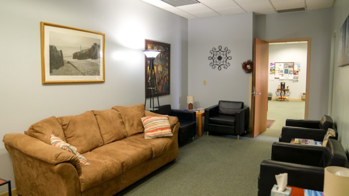 Interior lounge with tan sofa, black armchairs, framed artwork on walls, and connecting hallway to additional rooms