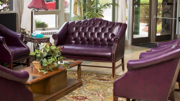 Interior lounge with purple leather furniture, glass doors accessing outdoors, potted plants, and natural light