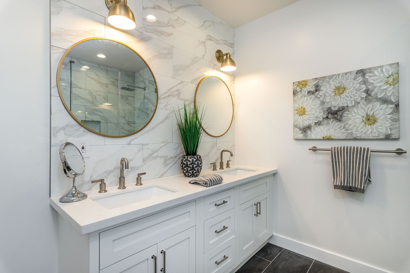 Interior bathroom with marble tile, dual round mirrors, white cabinetry, and brass pendant lighting