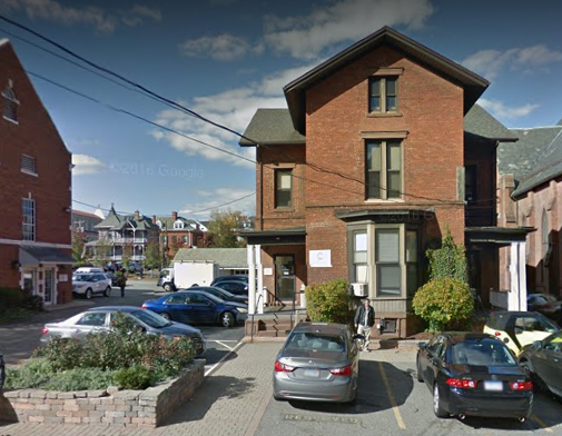 Exterior view of brick residential building with street parking, sidewalk, and neighboring structures.