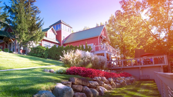 Exterior view of red barn-style building with metal roof, white trim, landscaped grounds with flowering shrubs and mature trees