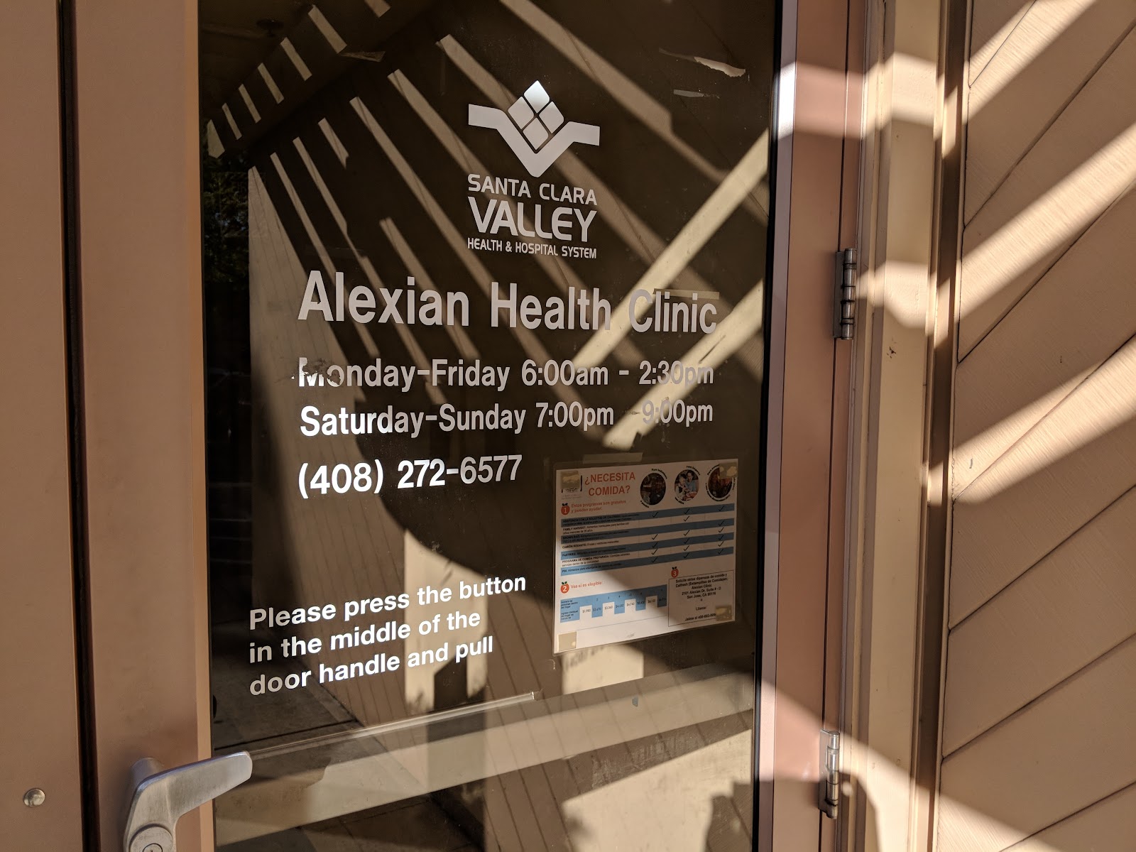 Glass entrance door displaying Alexian Health Clinic operating hours, phone contact information, and entry instructions.