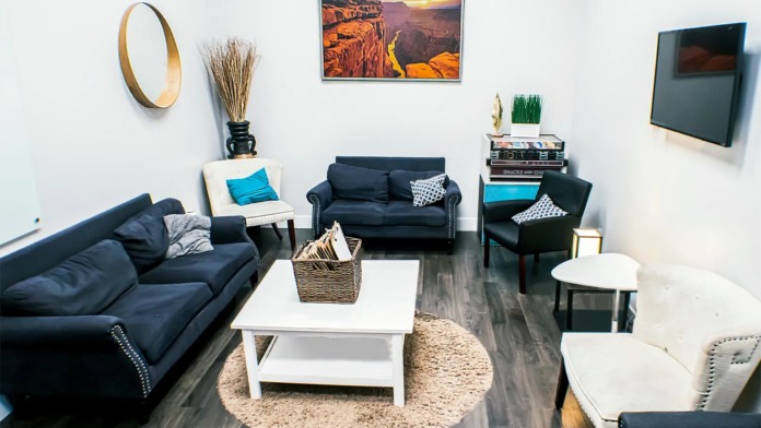Interior lounge with multiple blue sofas, white coffee table, and wall décor including mirror and landscape art.