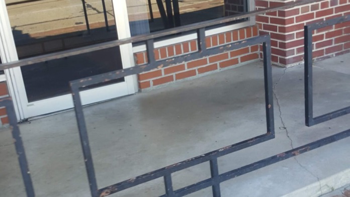 Exterior entrance door with notice signage, brick building facade, metal handrails, and glass entrance area